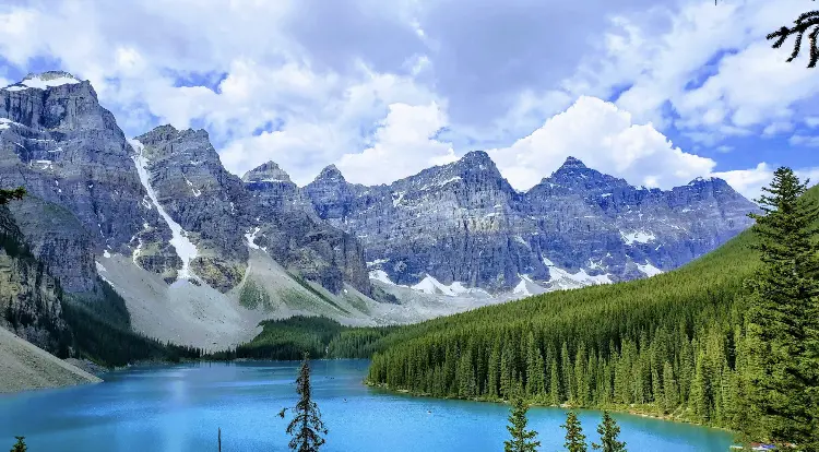 A mountain range with trees and water in the foreground.