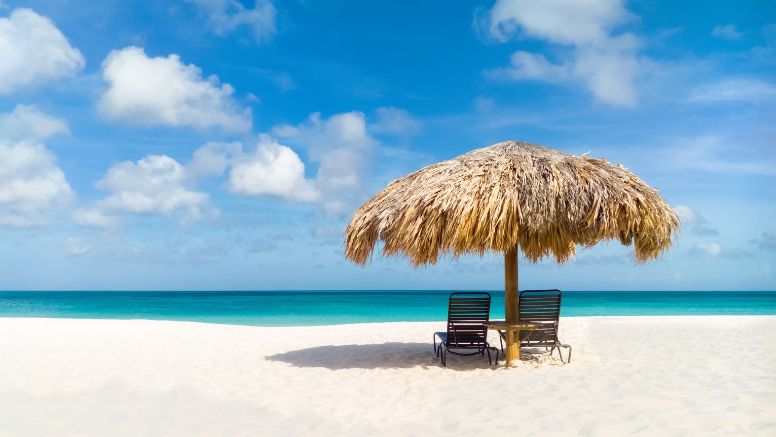 specializingin Two chairs under a straw umbrella on the beach.