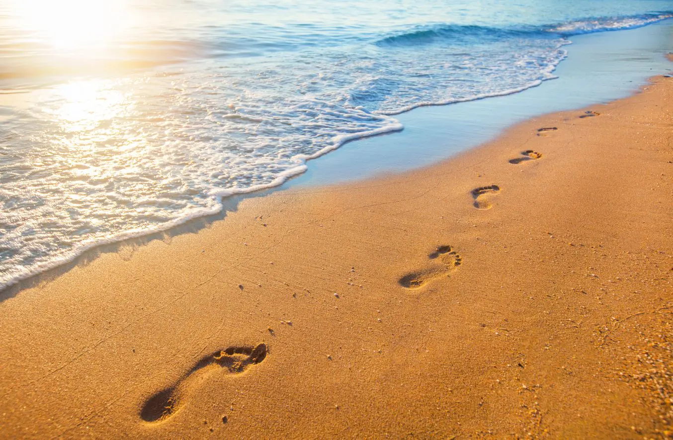 A beach with footprints in the sand and waves coming up.